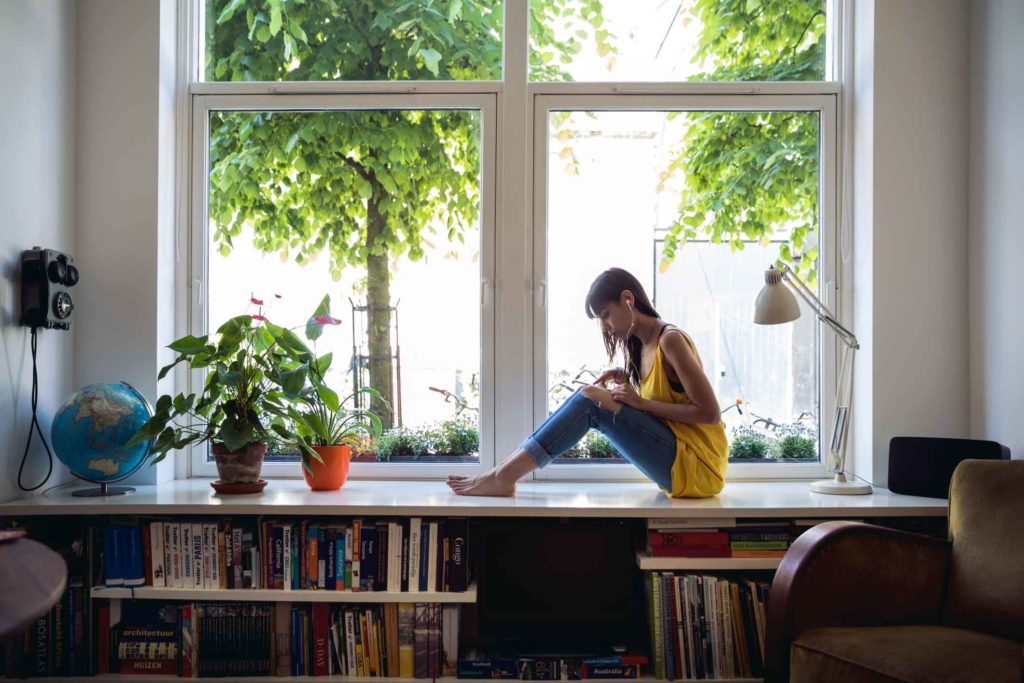 A sole trader sitting on her windowsill at home while sending invoices from her phone