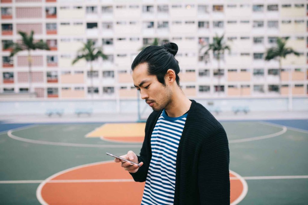A freelancer at an outdoor basketball court sending invoices on his phone