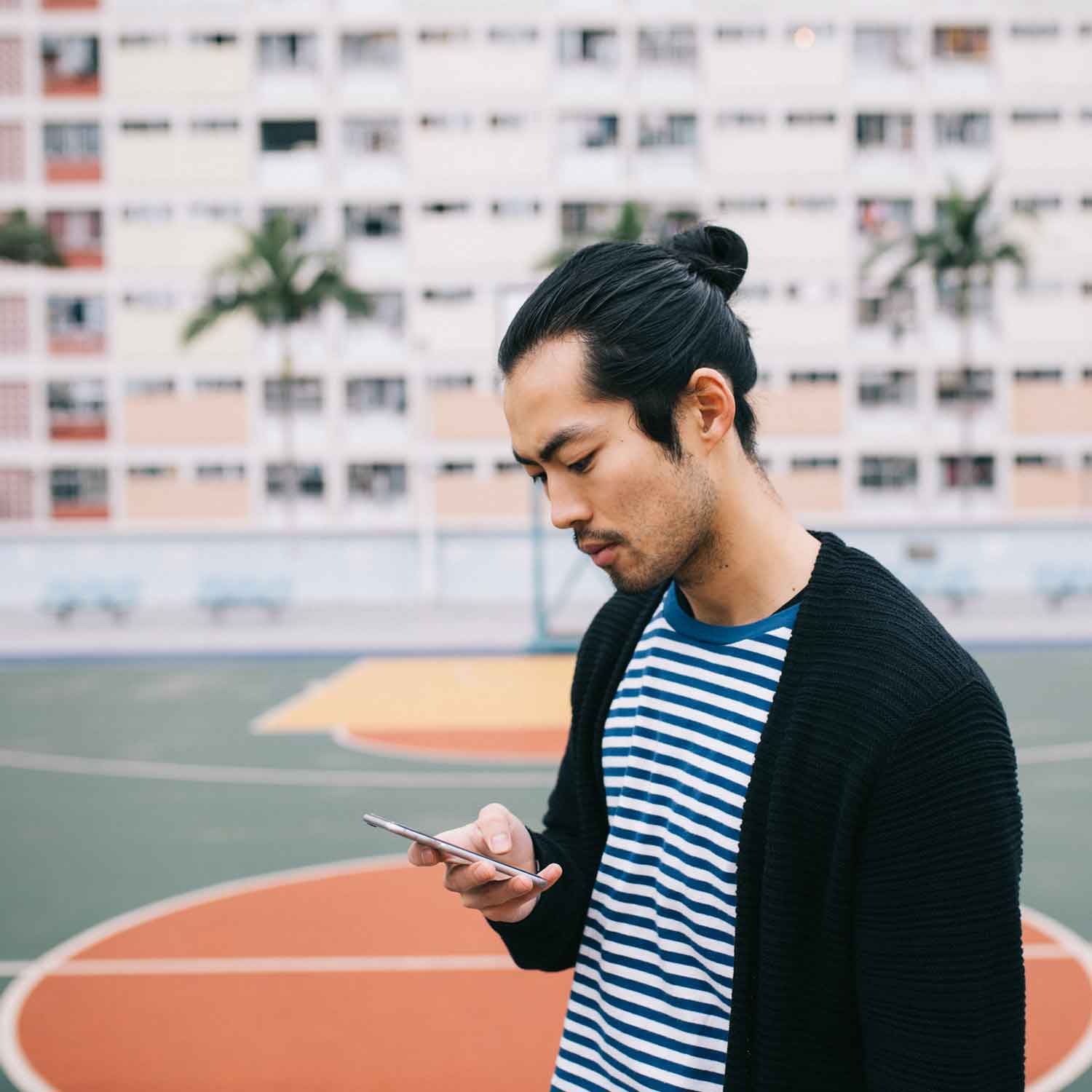 A freelancer at an outdoor basketball court sending invoices on his phone